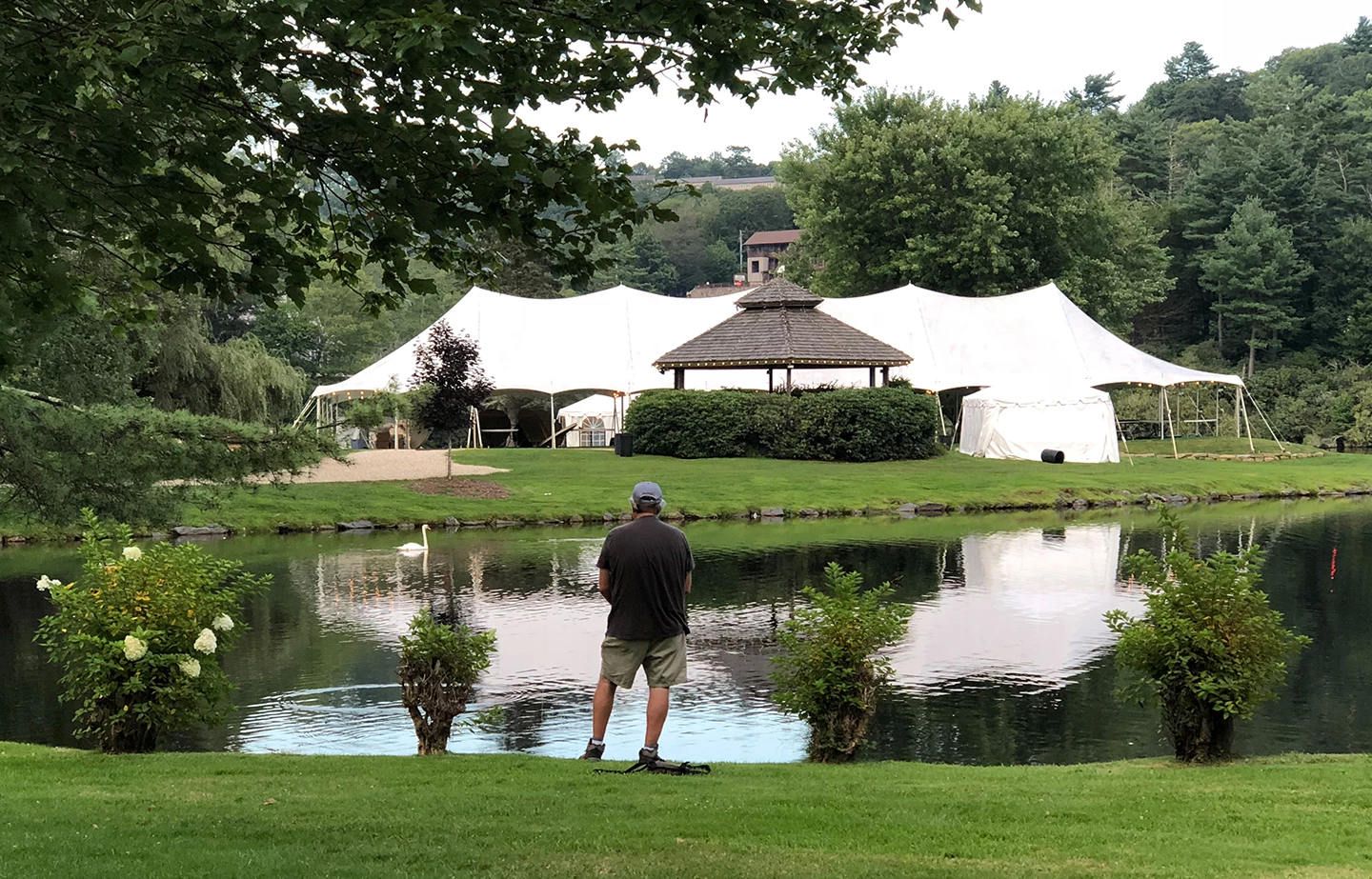 a man standing in front of a pond with a white tent