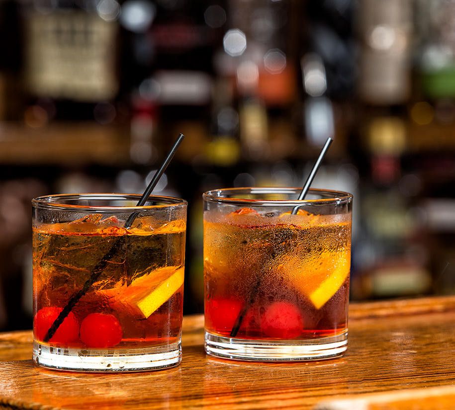two glasses with liquid and straws on a bar