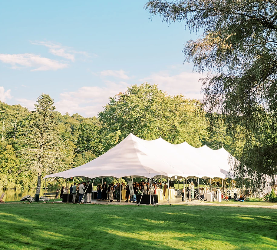 a white tent with people standing in front of trees