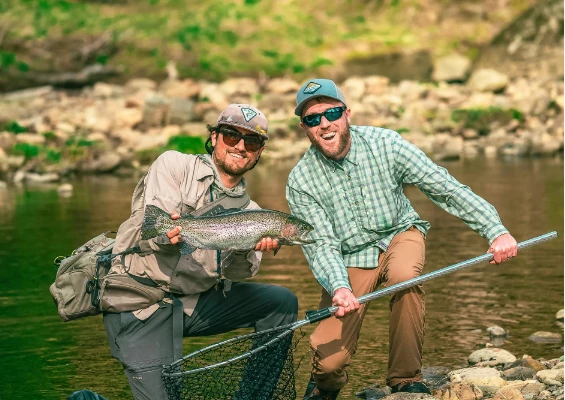 two men holding a fish and a net in a river