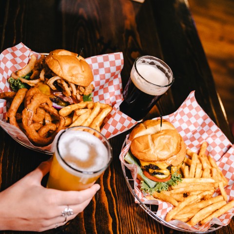 a hand holding a glass of beer and a plate of burgers