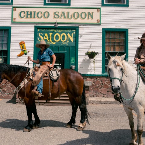 two people riding horses in front of a saloon.