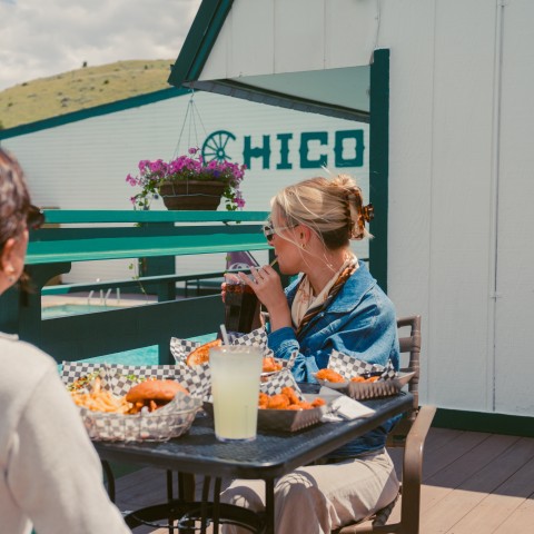 Two women sitting at a table with food and drinks.