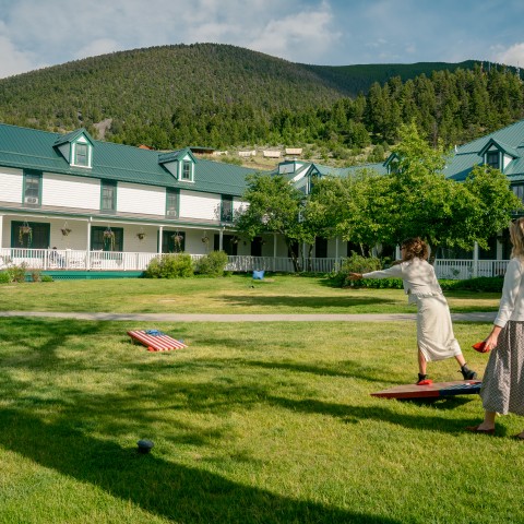 Two women standing in a yard playing cornhole.