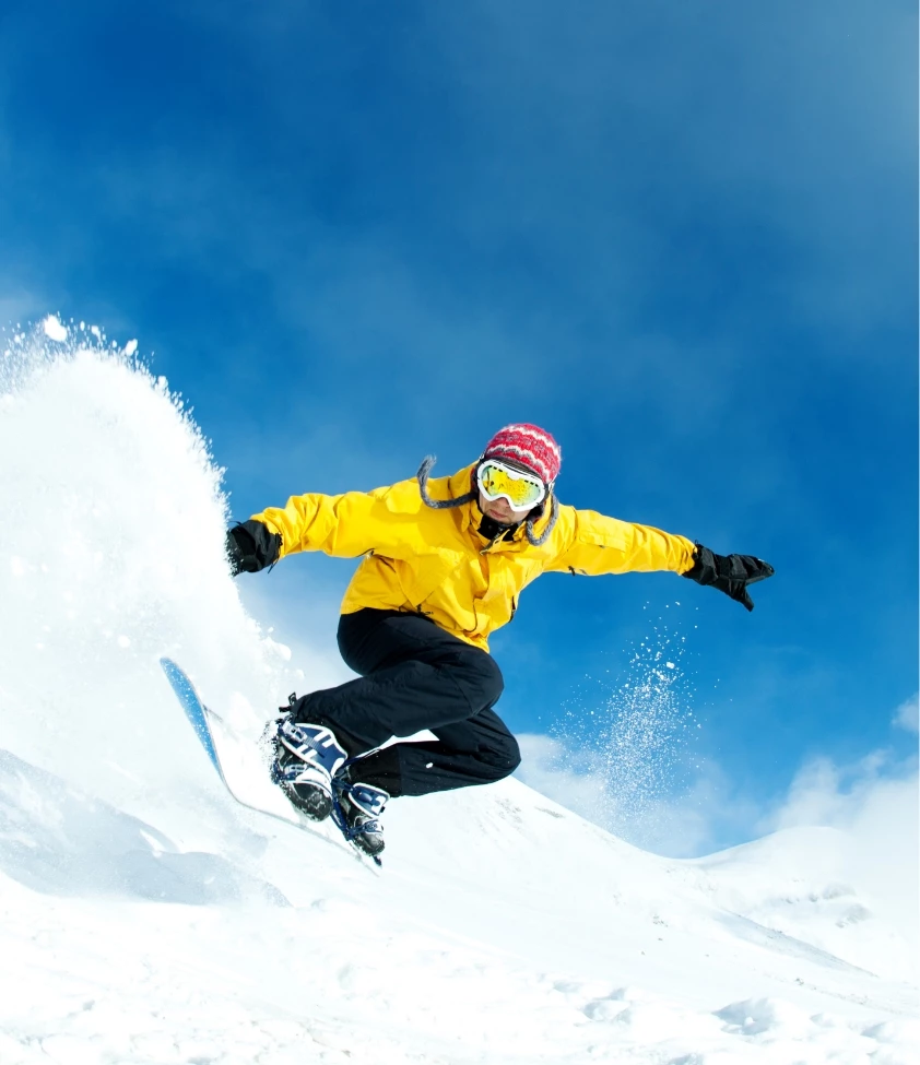 a person in a yellow jacket and goggles jumping on a snowboard