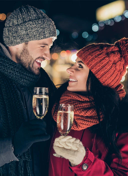 a man and woman wearing winter gear and holding glasses of champagne