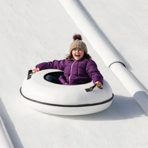 a little girl wearing snow gear while riding on a tube down the mountain