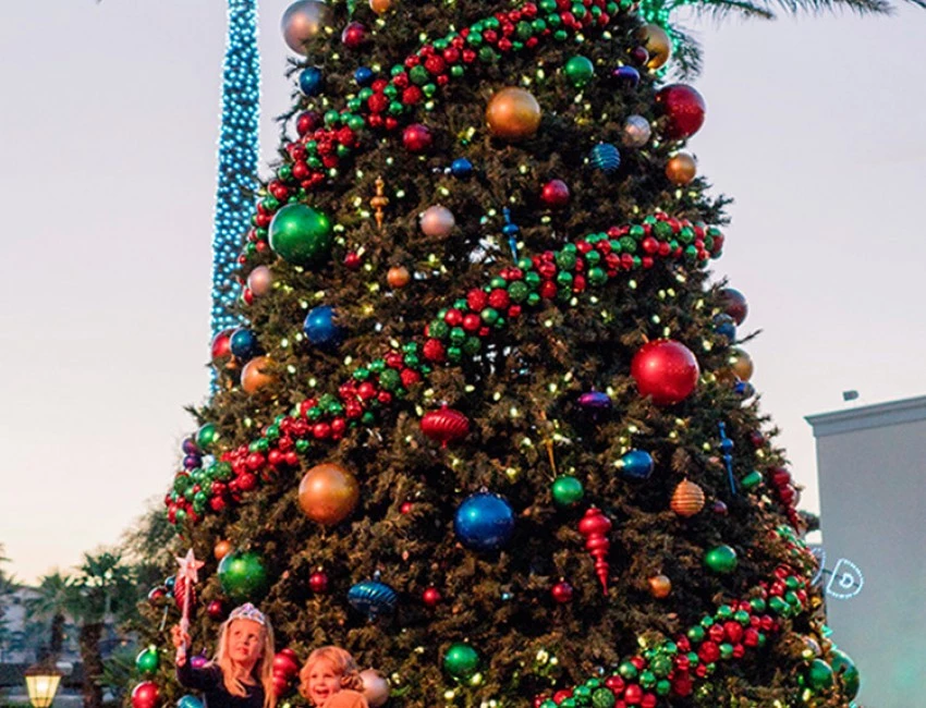 two little kids standing in front of a large christmas tree with lots of colorful decorations