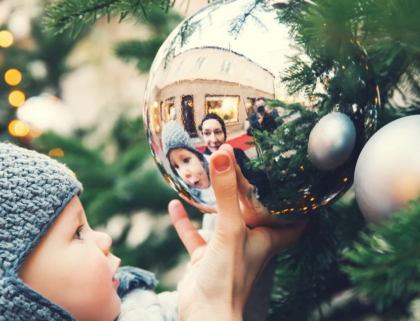 the reflection of a baby and its mom in an ornament on a tree