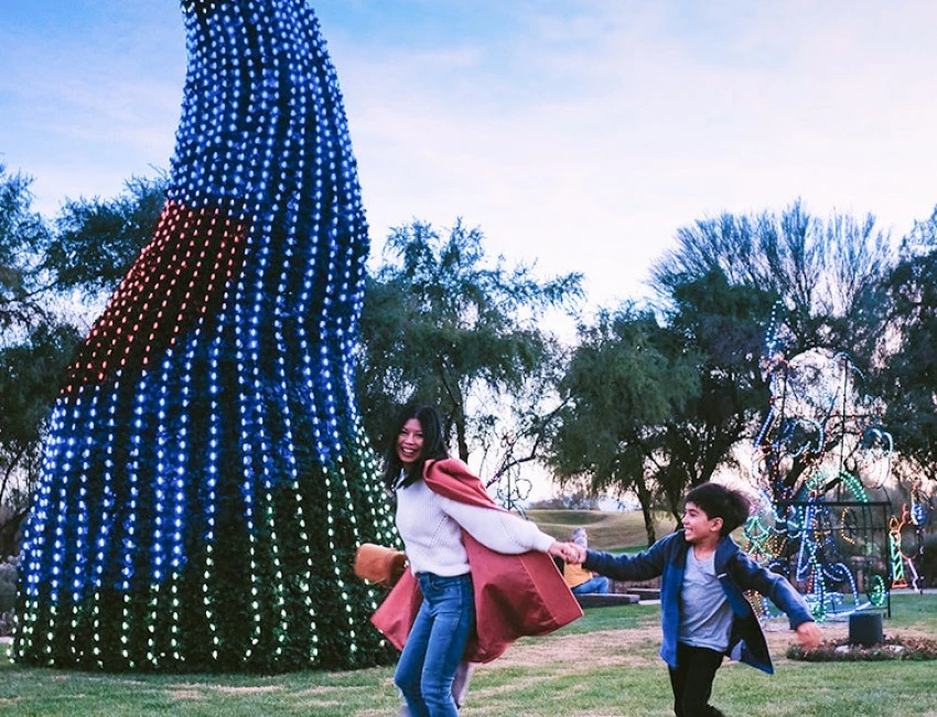 mother with a kid running on a field with a christmas tree behind