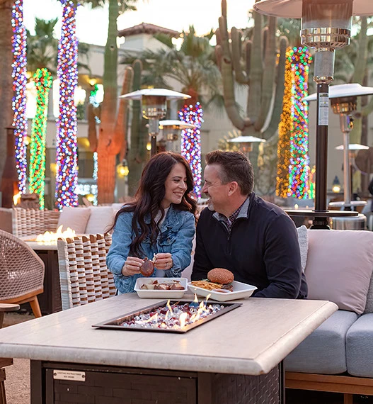 a man and woman sitting at a table with food and drinks