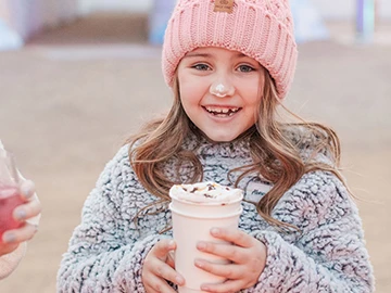 a young girl holding a drink with whipped cream on her nose
