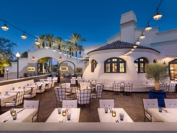 outdoor dining tables next to a modern designed white building at night