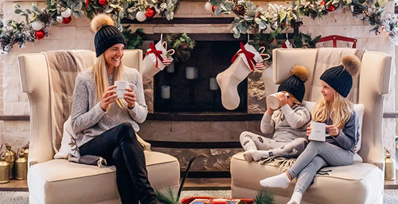 a woman with her two kids sitting and drinking her hot chocolate in front of a fire place