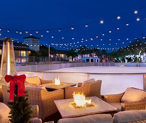 an area with lit fire pit and chairs next to the outdoor ice skating rink
