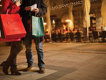 two people holding shopping bags while standing in front of people dining outside