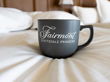 a fairmont princess black mug sitting on top of a bed