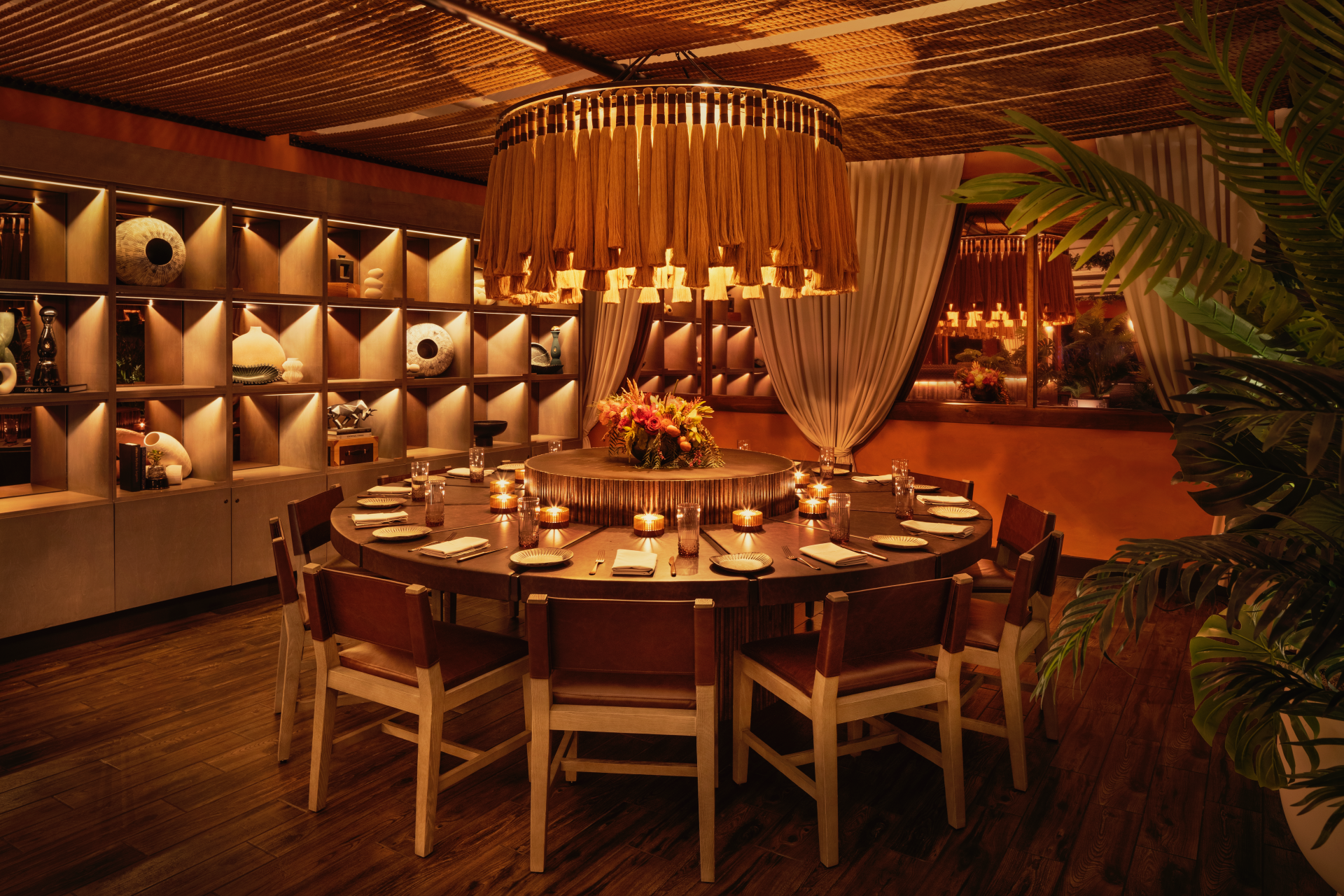 a round table with candles and chairs in a room with shelves and plants