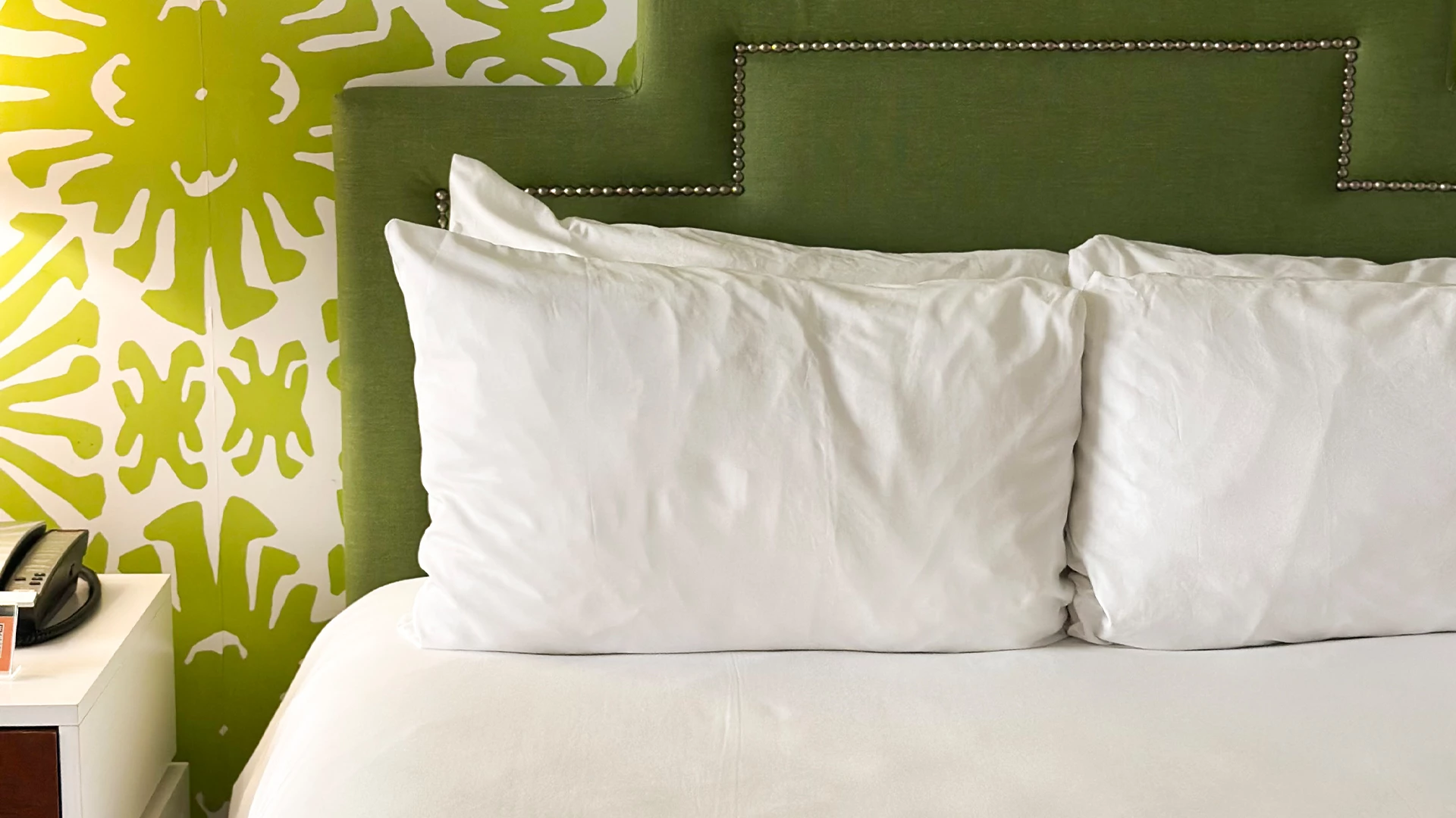 A close-up of a bed with a green headboard and white bedding