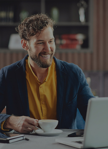 man taking a cup of coffee while looking at a laptop