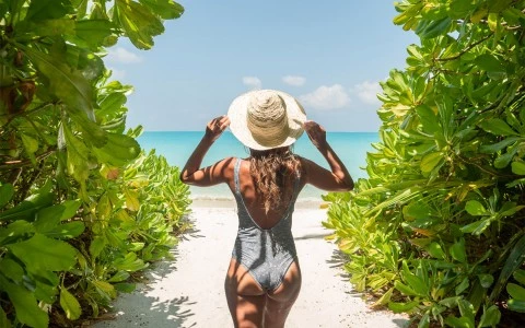 woman holding her hat in front of the beach