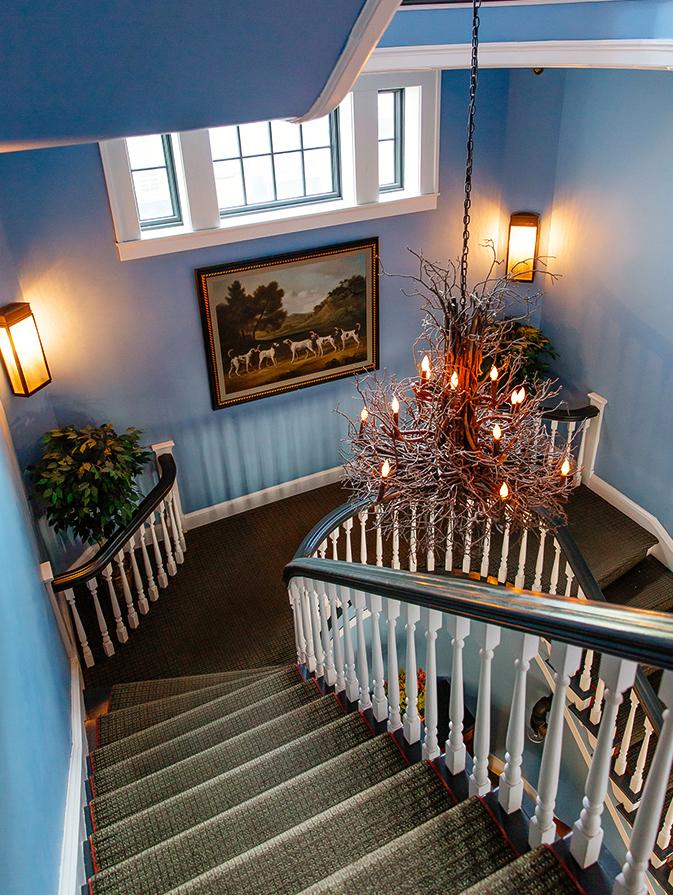a staircase with a chandelier and a painting on the wall