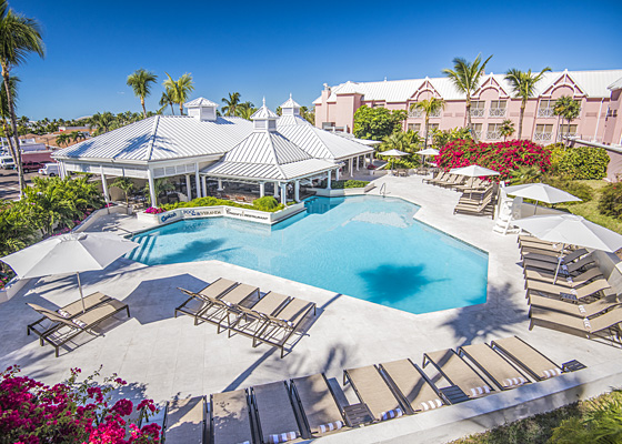 Aerial view of property with pink buildings enclosing pool area with white loungers