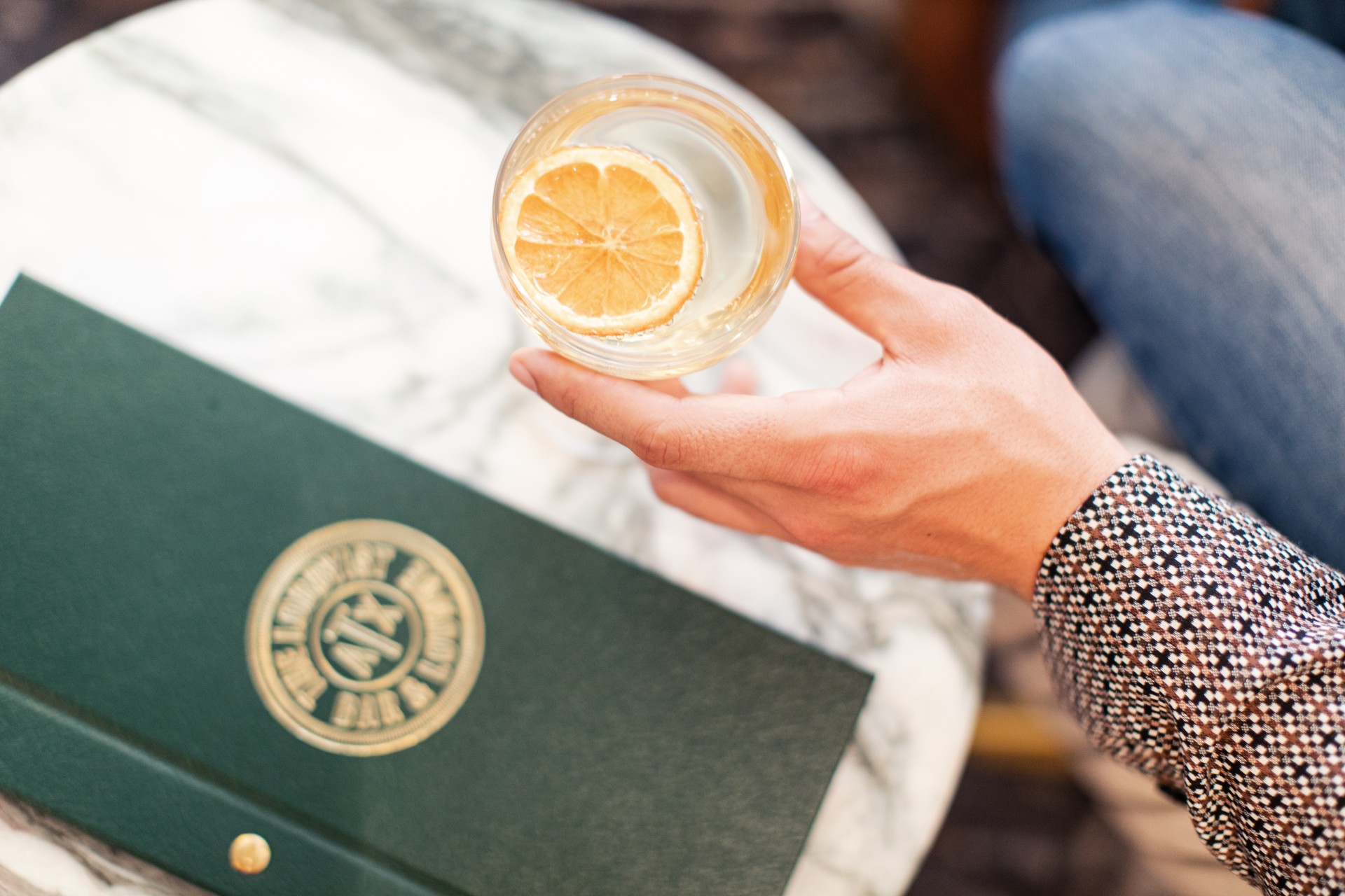 a person holding a glass of liquid with a slice of lemon