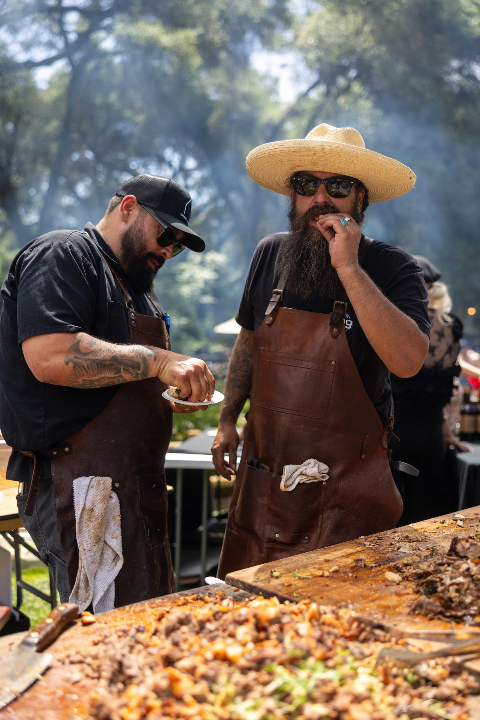 two men wearing aprons and hats standing next to a table with food