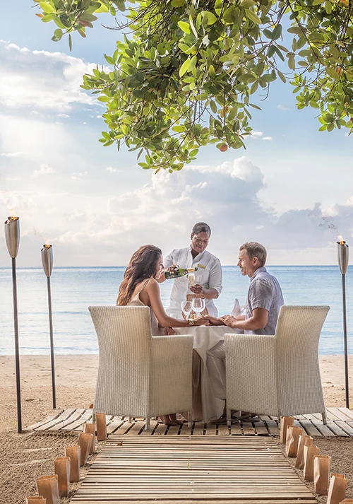 a group of people sitting at a table with wine glasses on a beach