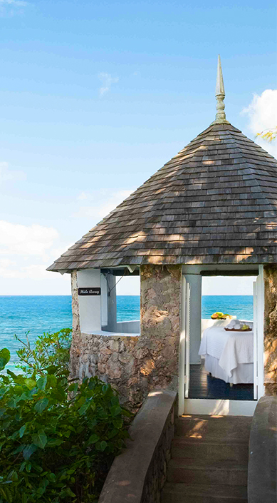 a stone gazebo with a bed and a body of water