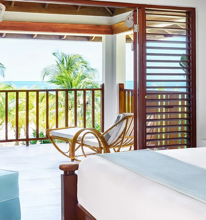 a room with a bed and a chair and a deck with a view of the ocean