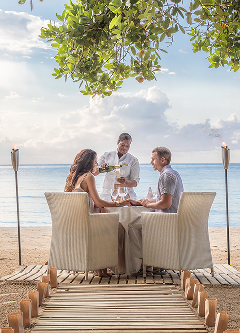 a group of people sitting at a table with wine glasses on the beach