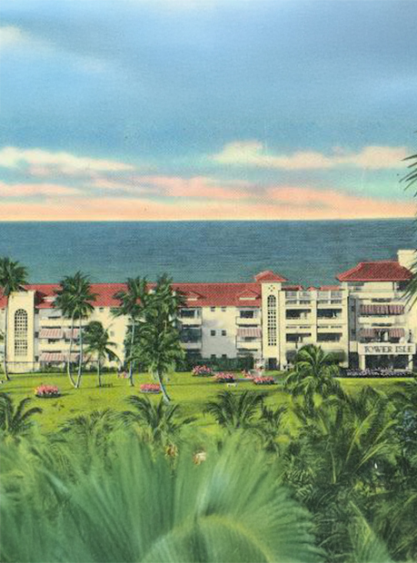 a large white building with palm trees and a lawn by the ocean