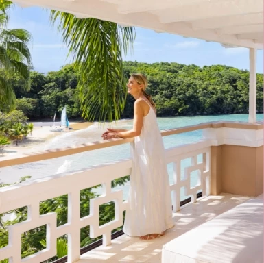a woman in a white dress standing on a balcony overlooking a body of water