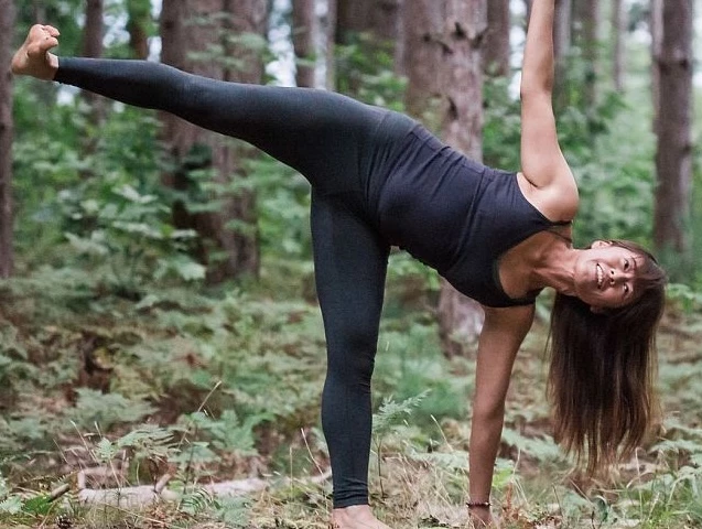 a woman in black clothes stretching in the woods