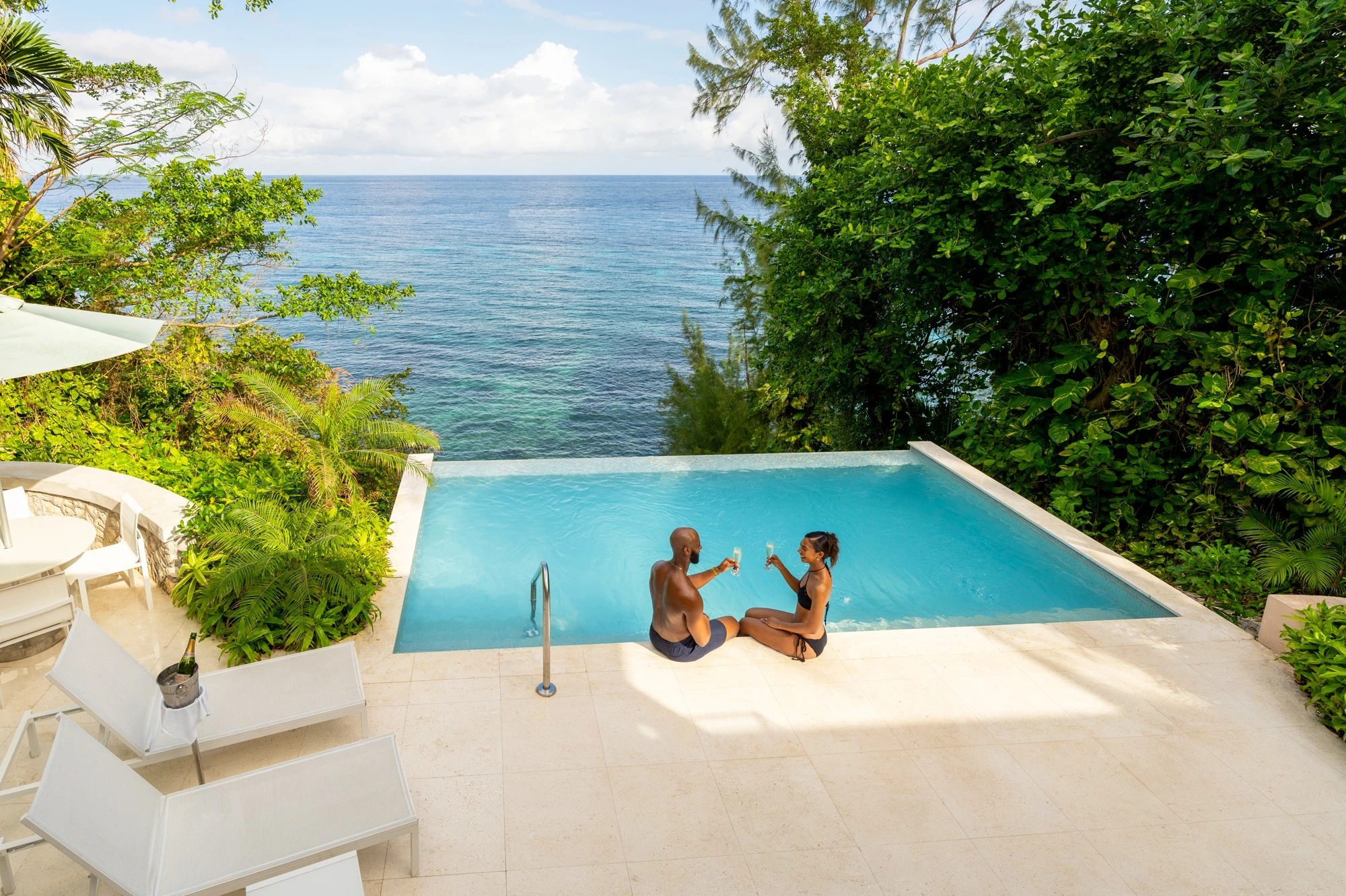 a man and woman sitting on a pool with a body of water