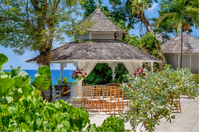 a gazebo with chairs and flowers in front of the ocean