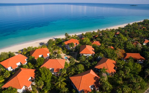 a group of houses with red roofs surrounded by trees and a body of water