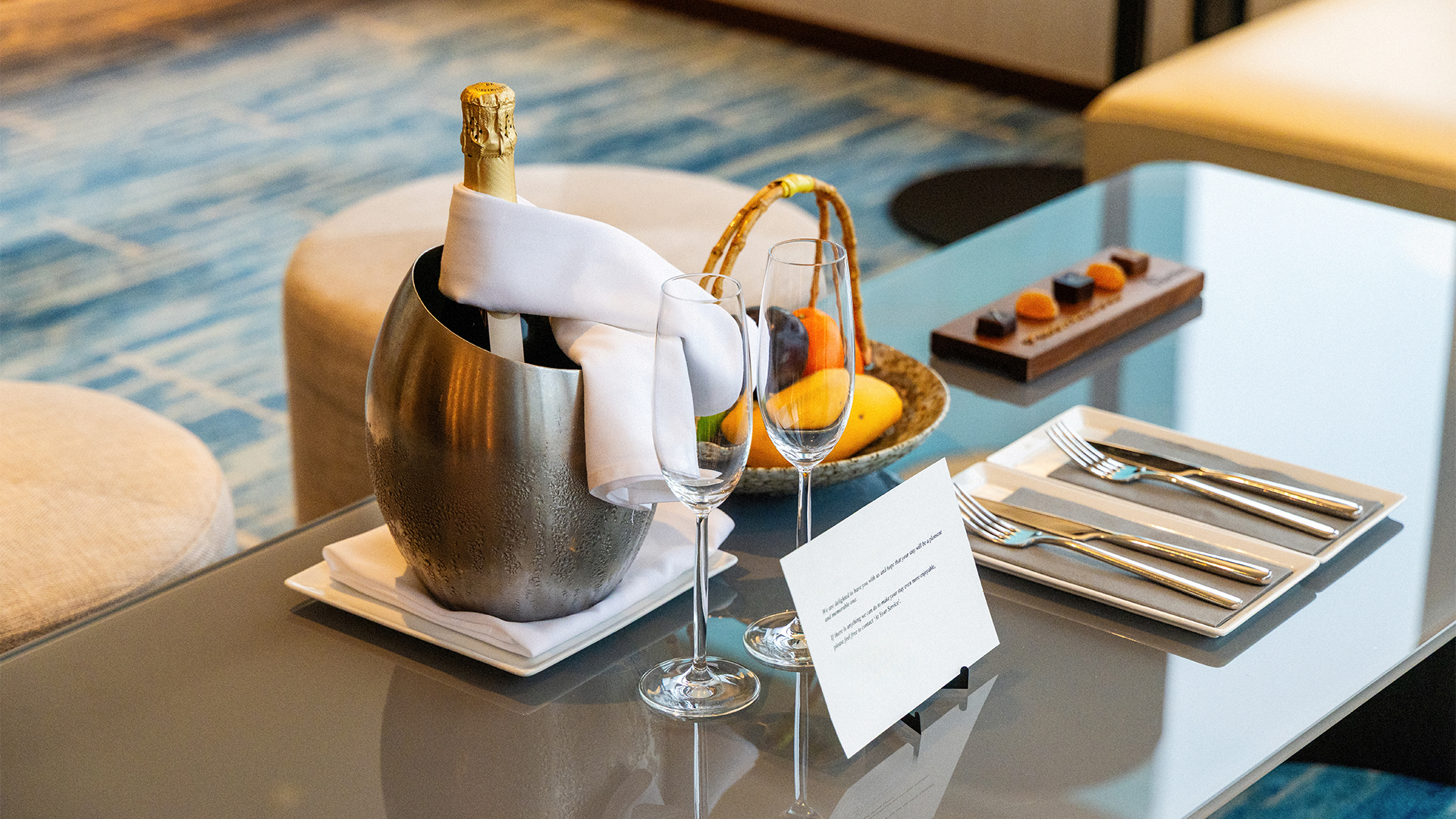a champagne bottle in a bucket with two wine glasses and a basket of fruit