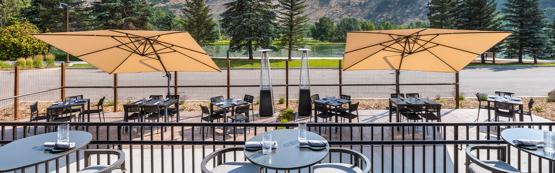 a table and chairs outside with a lake and mountains in the background