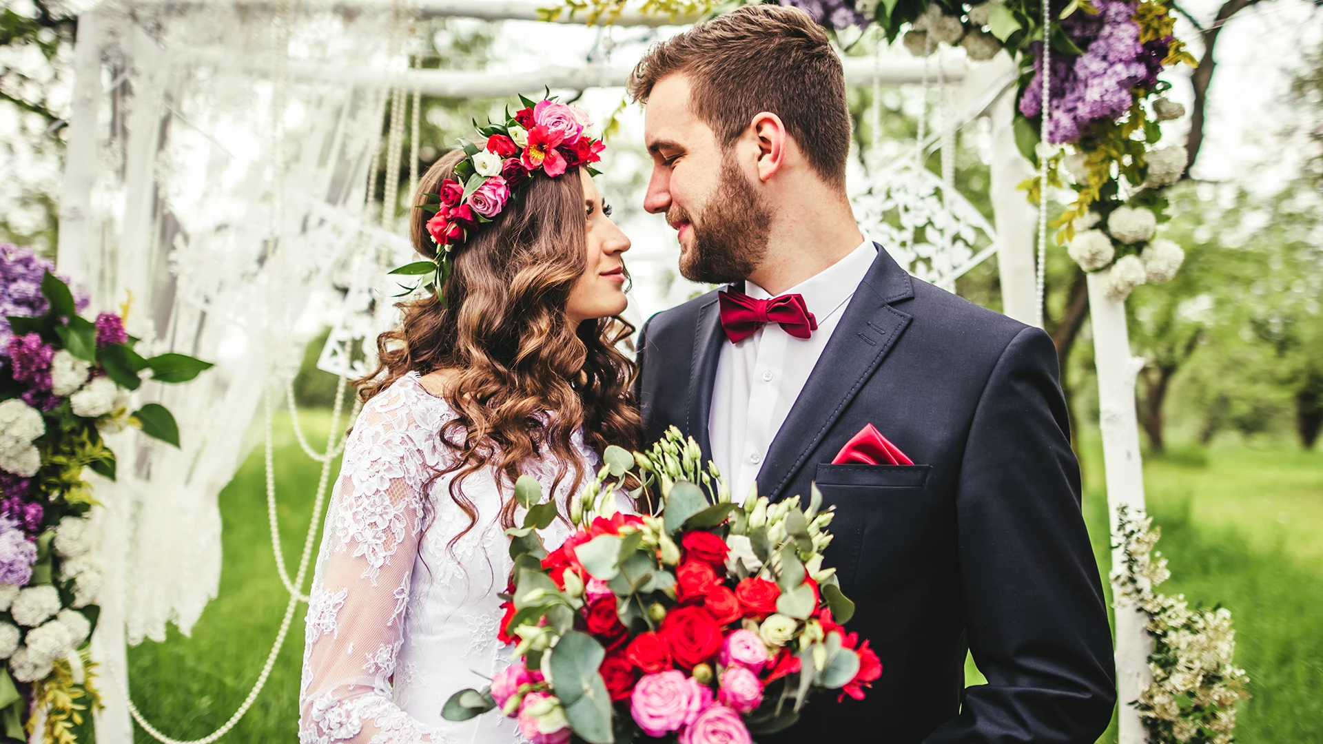 a man and woman in a wedding dress holding red and pink flowers 