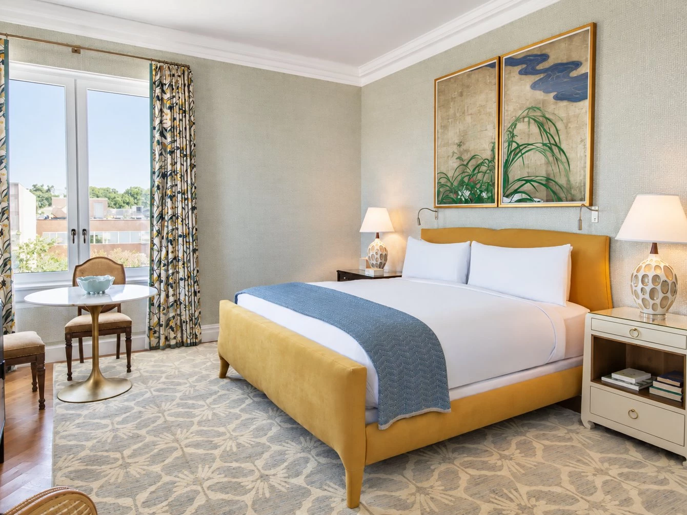 A hotel room with a yellow bed, white nightstands, and a window