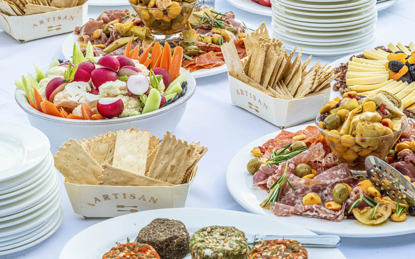 A table with various dishes of food including vegetables, meat, cheese, and crackers.
