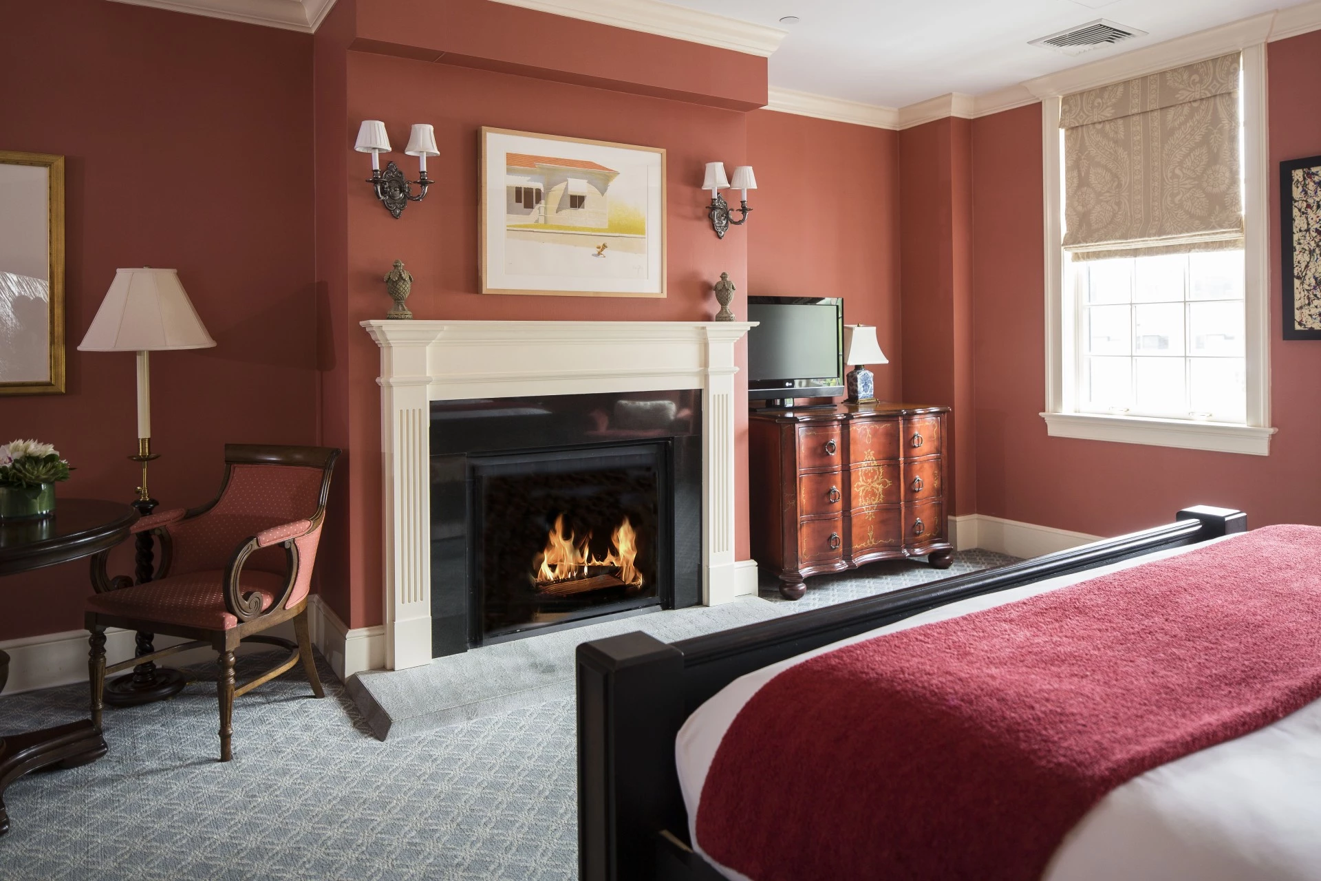 A cozy guest room with a fireplace, bed, chair, and window