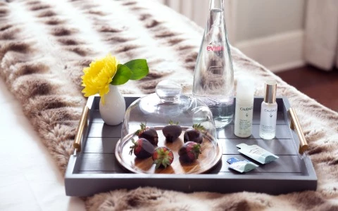 A tray with chocolates, flowers, and skincare products on a bed