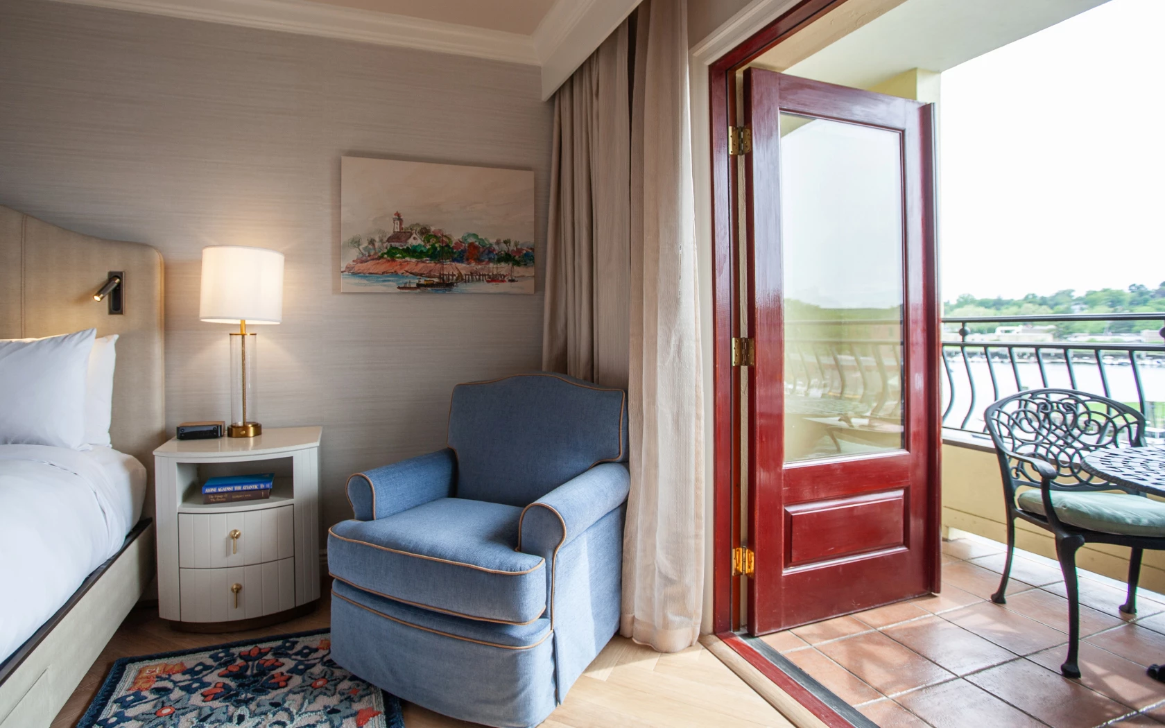 A hotel room with a bed, chair, lamp, and balcony with a view.