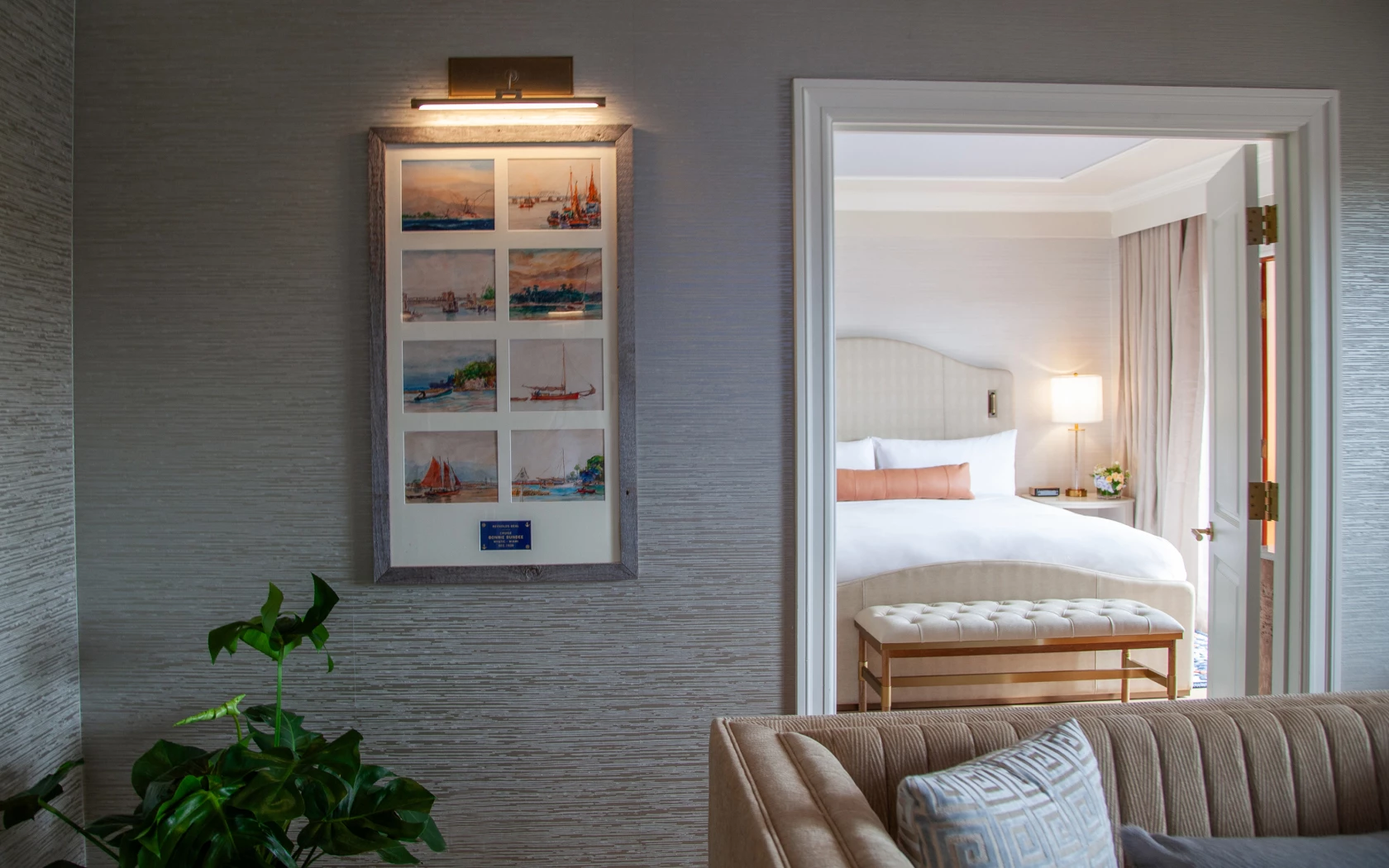A hotel room with a partially open door revealing a bed and a sitting area with a couch and artwork.