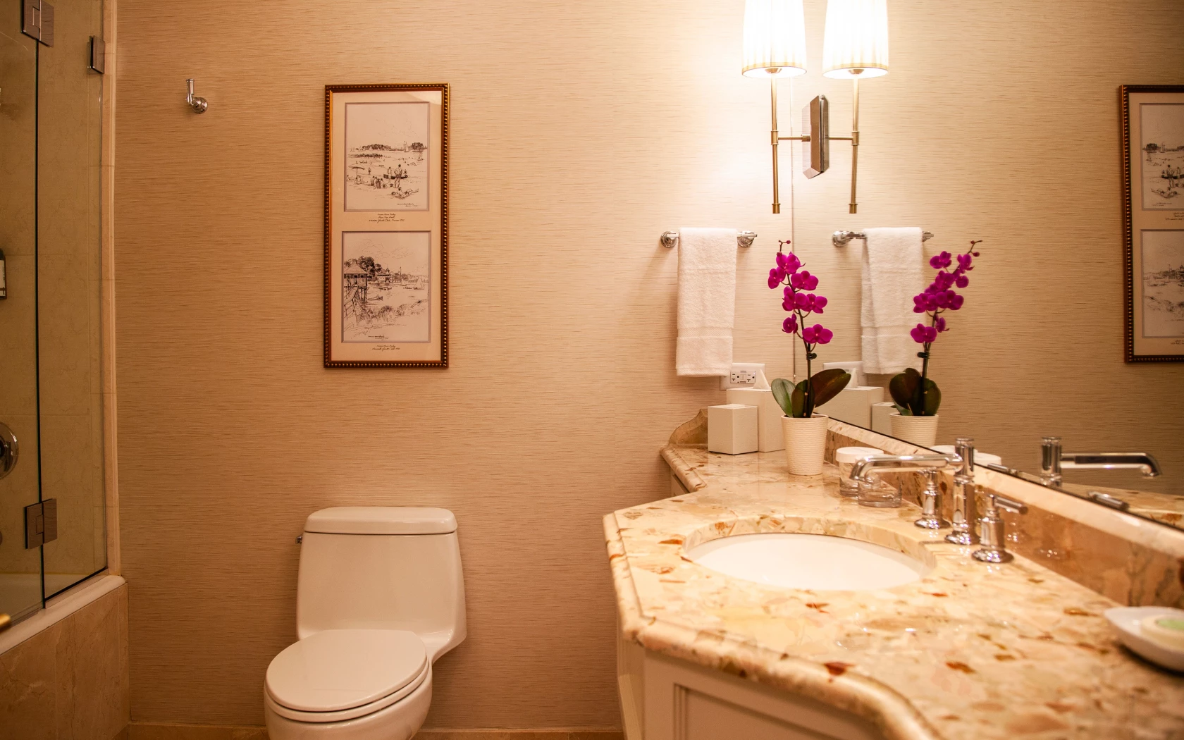 A bathroom with a marble countertop, double vanity, and pink orchids