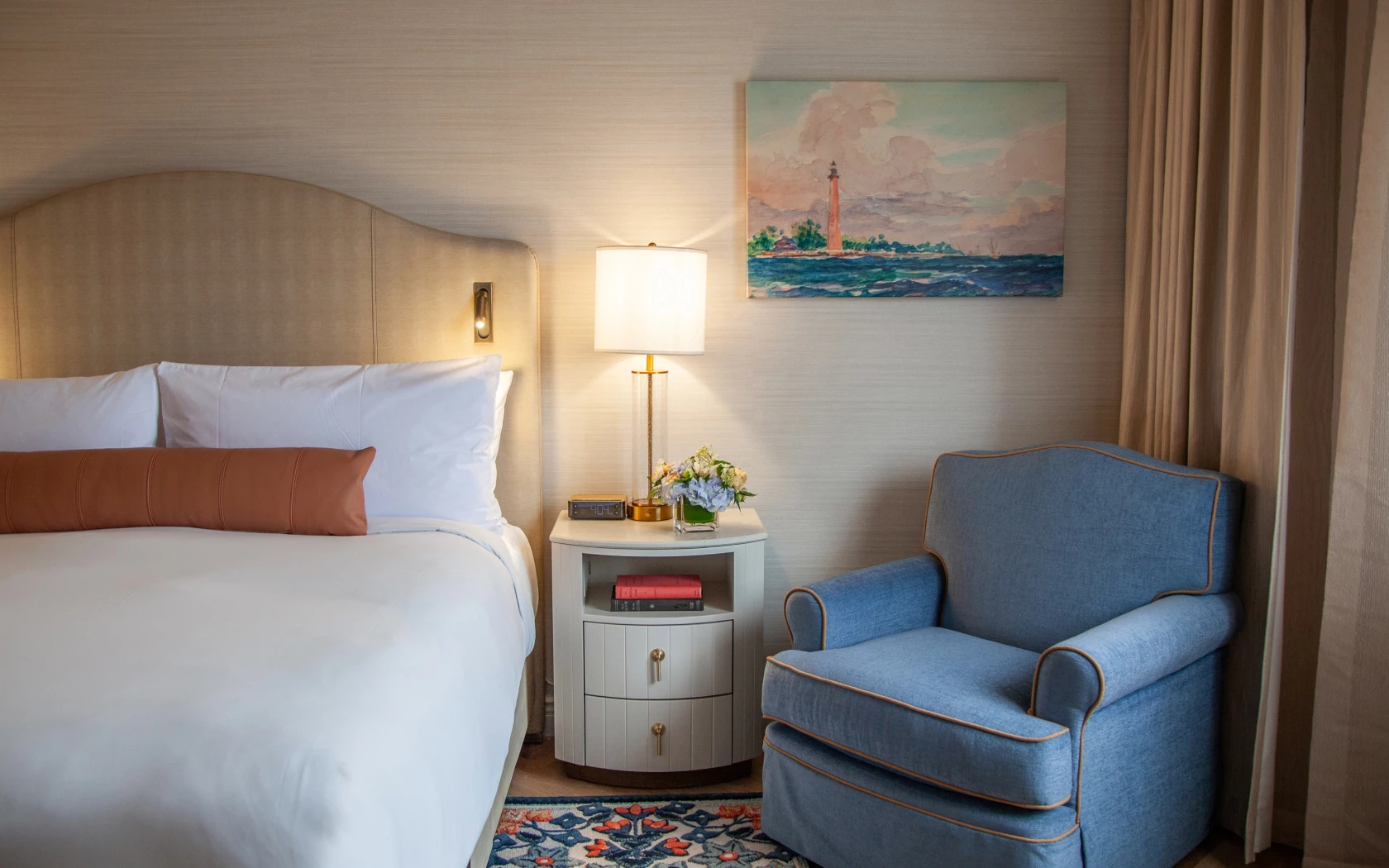 A hotel room with a bed, chair, lamp, and nightstand.
